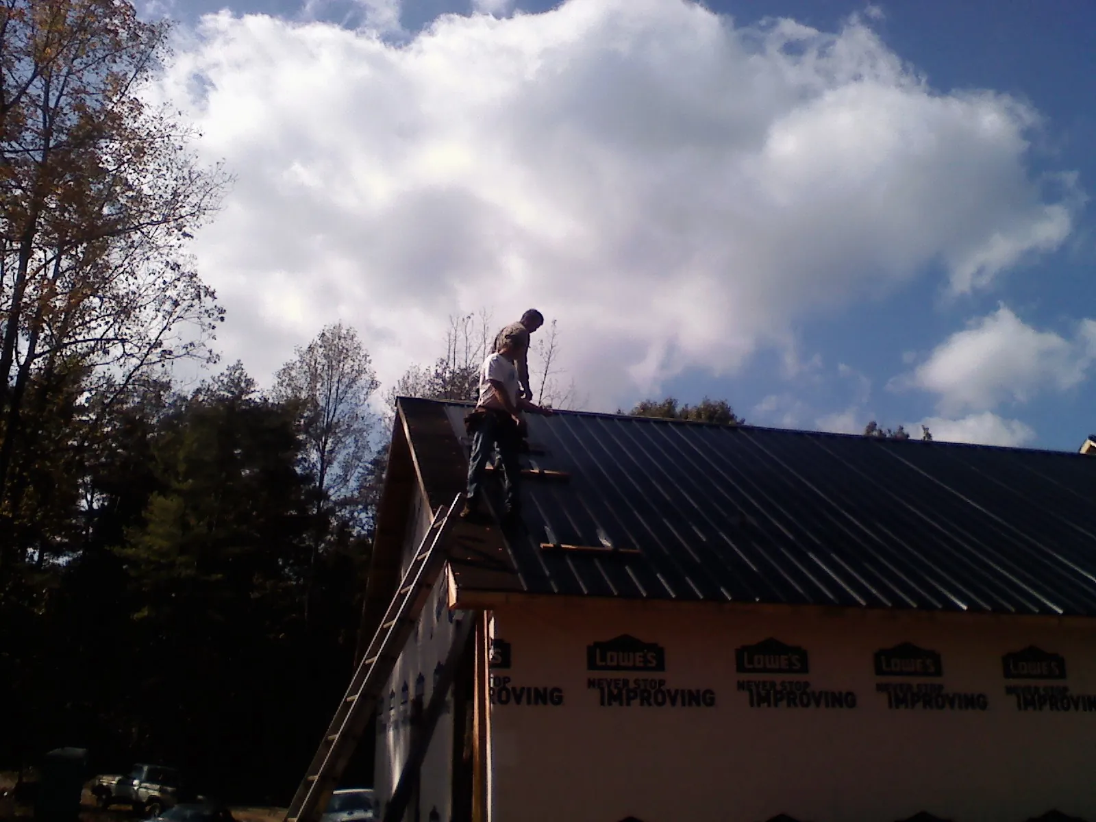 Roofer fastening dark metal panels high against a cloudy sky, from a Roof Inspection job in Allenhurst
