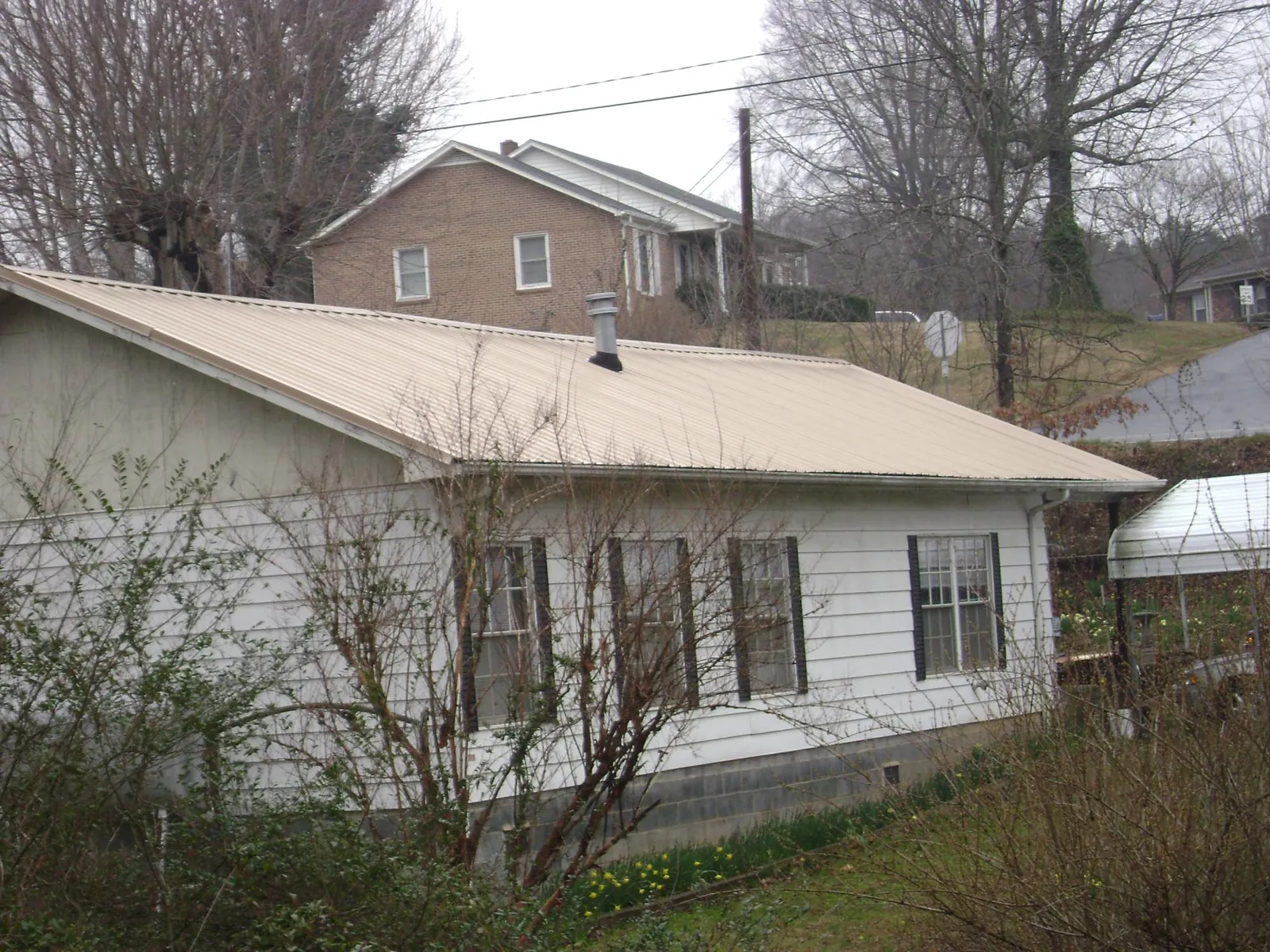 Tan metal roof on a white sided house set into a hillside — Commercial Roofing by Roofing Brothers in Allenhurst